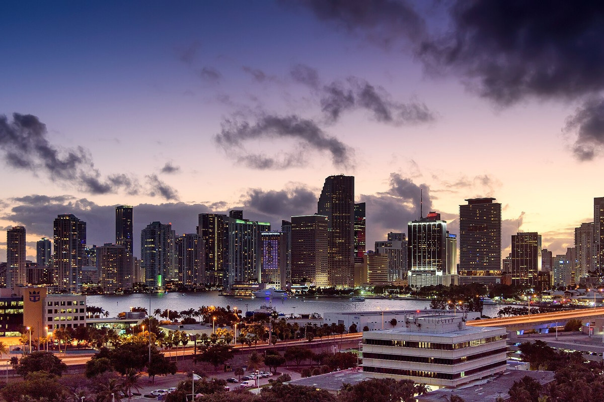 Mainland Miami skyline and illuminated waterfront beneath a violet dusk sky, viewed from PortMiami