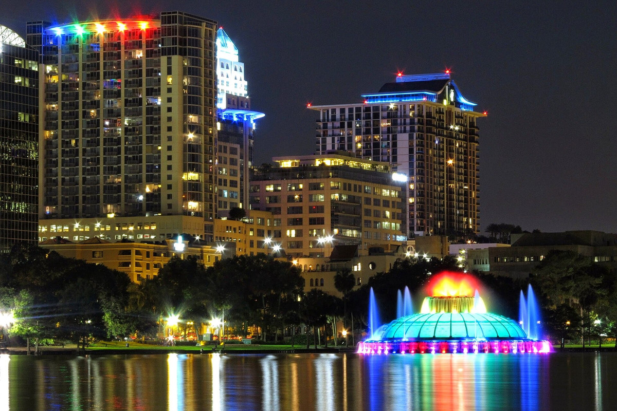 Colorfully illuminated Lake Eola fountain and Orlando buildings reflected in the lake at night