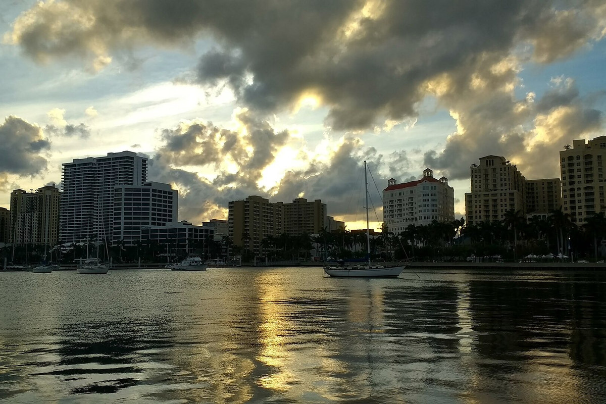 West Palm Beach waterfront buildings reflected in water beneath golden sunset clouds