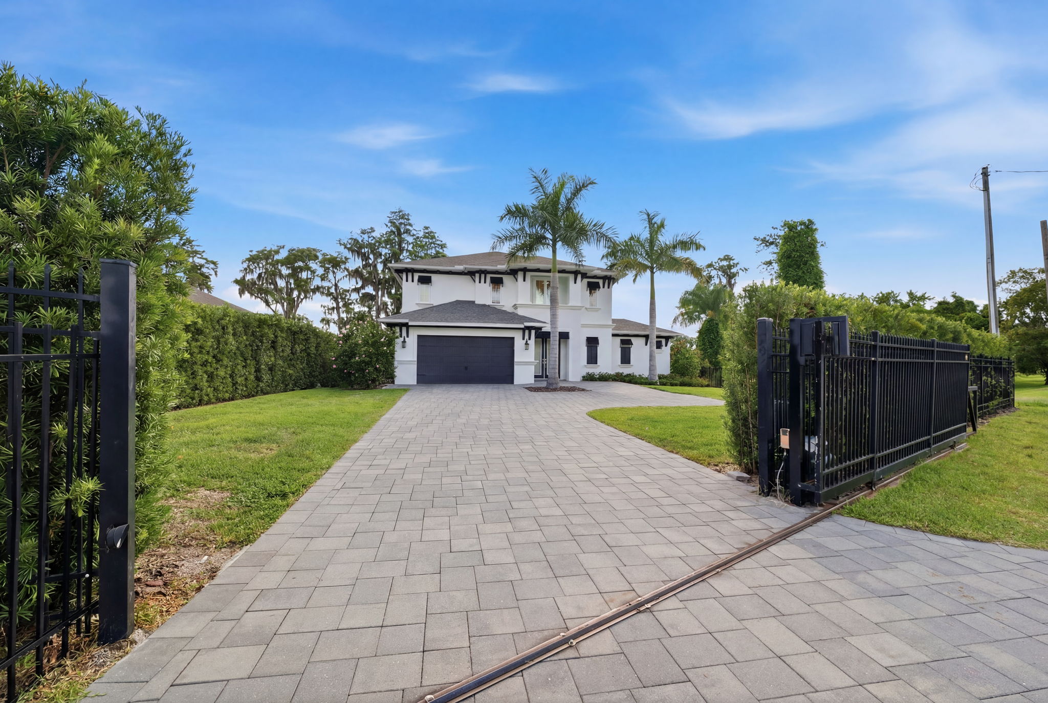 White two-story home behind an open black gate and broad paved driveway