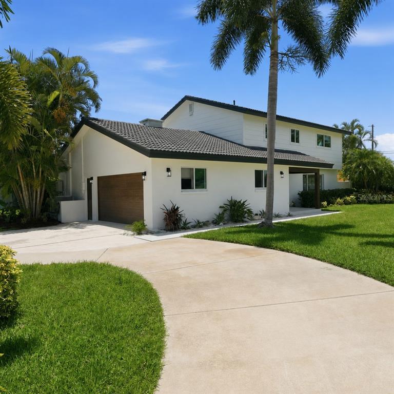White two-story home with a garage, curved driveway and palm trees
