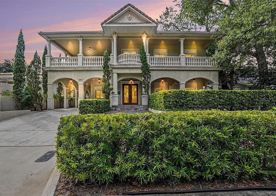 Two-story classical-style home with balconies, columns and landscaping at dusk